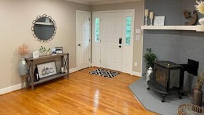 A living room with wooden flooring, a fireplace, a mirror, and a door with frosted glass panels. - License To Chill - Lakefront/Screened in Porch (Bumpass)