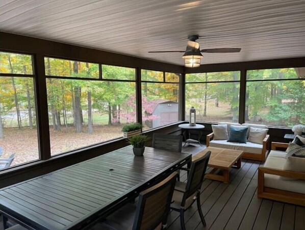 A covered outdoor seating area with a table and chairs, large windows, and a ceiling fan.