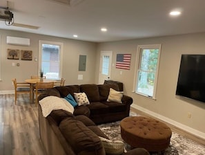 A living room with a sectional sofa, ottoman, and a dining area with a table and chairs.