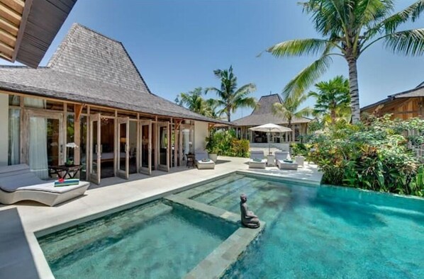Relax by the pool in a serene tropical setting, surrounded by lush greenery and a thatched roof.