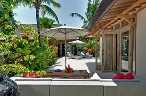 Relax in a serene outdoor space surrounded by lush greenery and palm trees, with a covered seating area and lounge chairs.