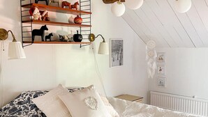 Een slaapkamer met een bed, kussens, een plankje met beeldjes, een dreamcatcher en wanddecoratie.