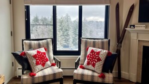 A room with two armchairs facing a large window, a sign above the window reading "Almost Heaven West Virginia", and a fireplace to the right. - Ski In/out, Sleeps 8, Pool, Hot Tub, Snow Tubing! (Snowshoe)