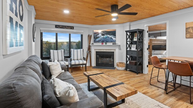 A modern living room with a fireplace, a dining area, and a view of a snowy landscape through large windows. - Ski In/out, Sleeps 8, Pool, Hot Tub, Snow Tubing! (Snowshoe)