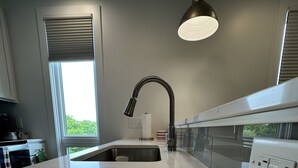 Una cocina moderna con encimera de mármol blanco, un lavamanos de acero inoxidable y una lámpara colgante.