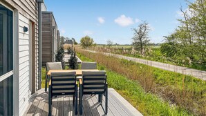 A deck with a table and chairs, overlooking a grassy area and a road. - Beautiful home in Tossens with sauna (Tossens)