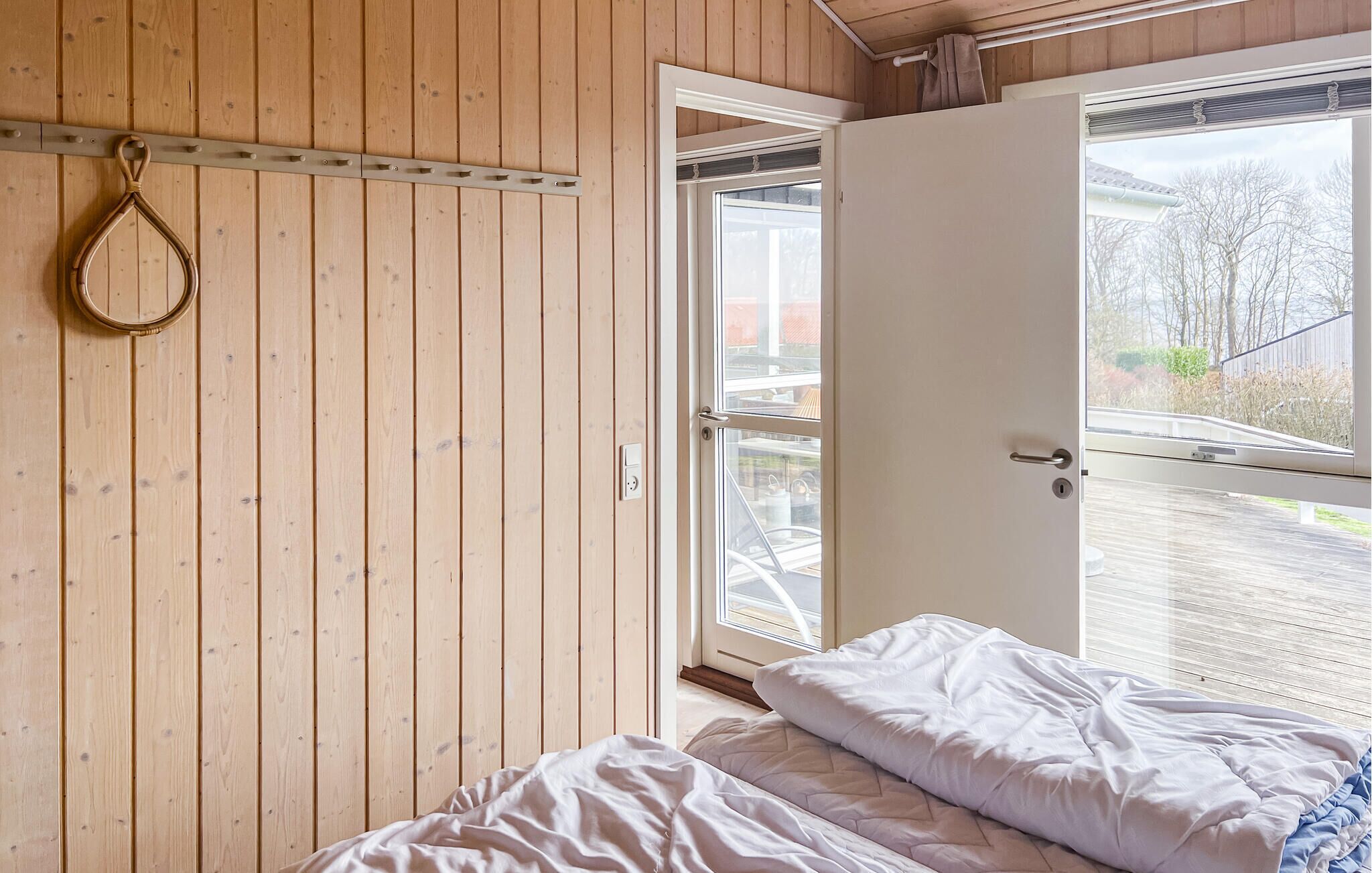 Una habitación con paneles de madera, una cama con ropa de cama blanca, una puerta que da al exterior y una ventana con vistas al exterior.