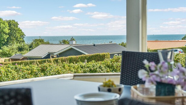 A dining table with plates and a vase of flowers, overlooking a coastal view with houses and a clear sky. - Awesome home in Sydals with kitchen (Sydals)