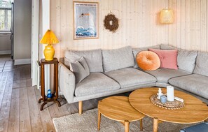 A modern living room with a grey sectional sofa, a small wooden side table with a yellow lamp, a round wooden coffee table, and a framed poster on the wall.