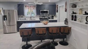 A modern kitchen with dark cabinets, a stainless steel refrigerator, a microwave, and a large island with bar stools.