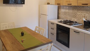 A compact kitchen with wooden cabinets, a built-in stove, and a refrigerator. - Cozy Little House in town La Ficurinia 🌵 (Siracusa)