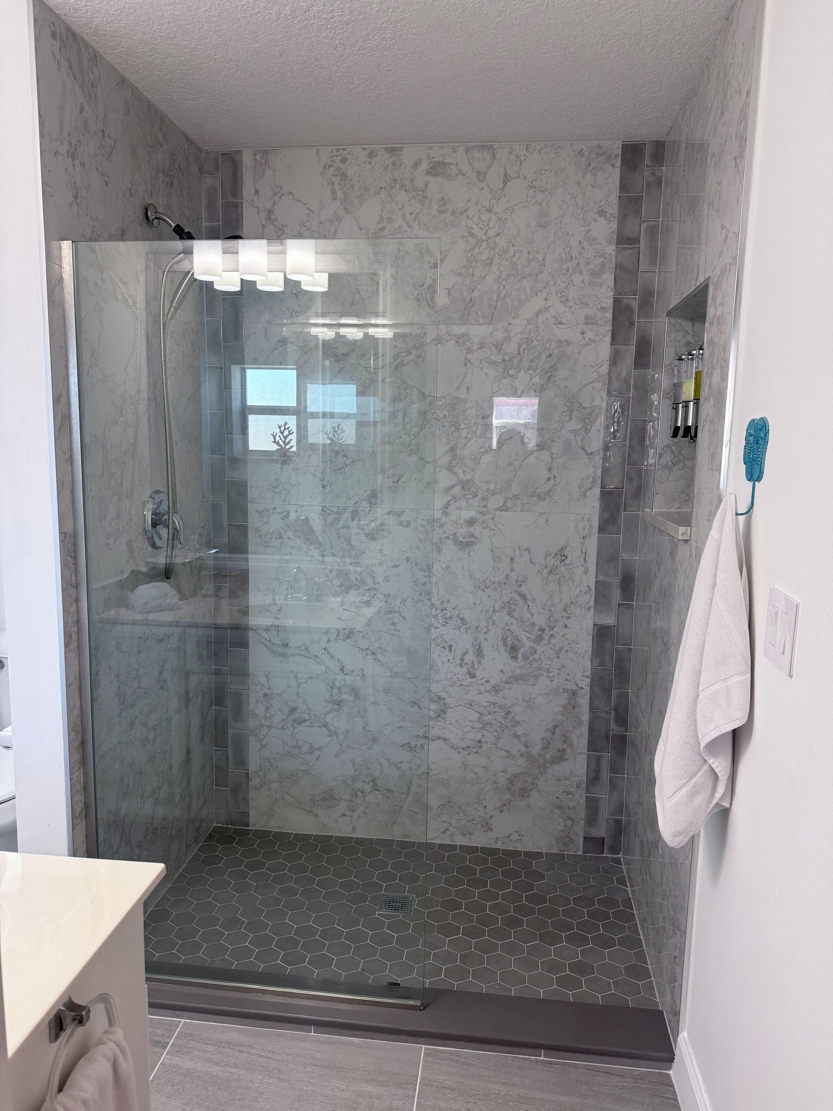 A glass-enclosed shower with a marble wall, a white towel hanging on the wall, and a visible showerhead.