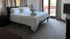 Een netjes opgemaakt bed met witte lakens, een plafondventilator, een airconditioning, een klein tafeltje met een vaas en een balkon met uitzicht.