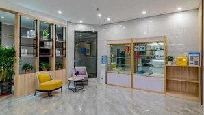 Un vestíbulo moderno con piso de mármol, un sillón amarillo, una mesita redonda y una vitrina de vidrio con objetos.
