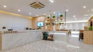 Una moderna zona de recepción de hotel con suelo de mármol, un mostrador de recepción, una pantalla de televisión y una exhibición de plantas.