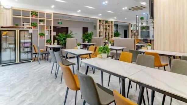 Un comedor moderno con mesas y sillas, estanterías con plantas y un refrigerador.