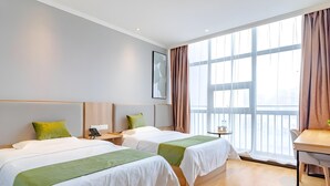 Habitación de hotel con dos camas, un escritorio y un ventanal grande con cortinas.