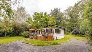 Una cabaña pequeña de un solo piso con terraza de madera y zona de estar cubierta al aire libre.