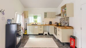 Cocina compacta con refrigerador, lavamanos y estufa. Hay un taburete pequeño y un extintor cerca de la puerta.