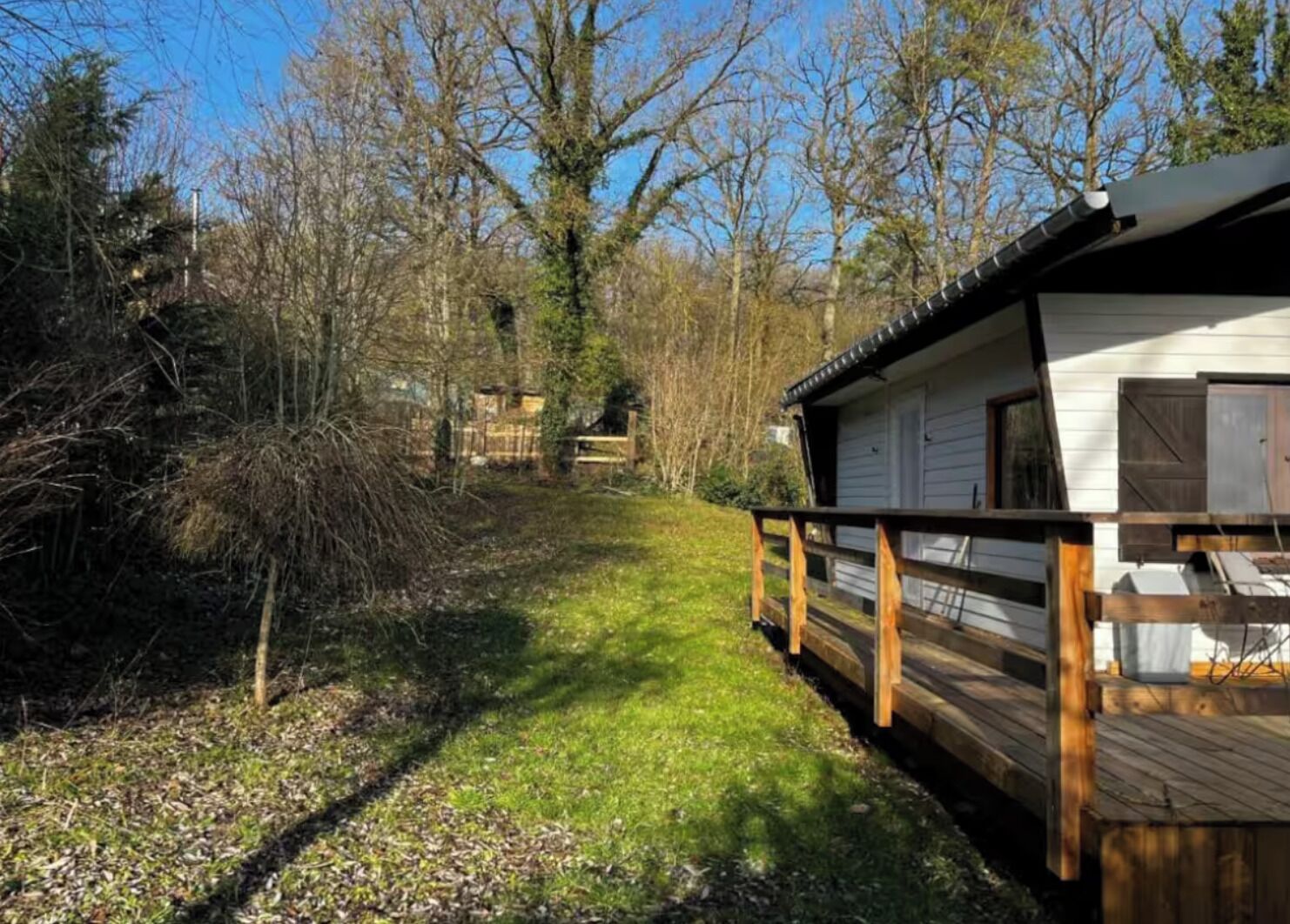 Eine Holzdielenfläche führt zu einer Hütte mit Garage, umgeben von Bäumen und einer Rasenfläche.