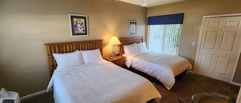 A hotel room with two beds, a bedside table with a lamp, a ceiling fan, and a door.