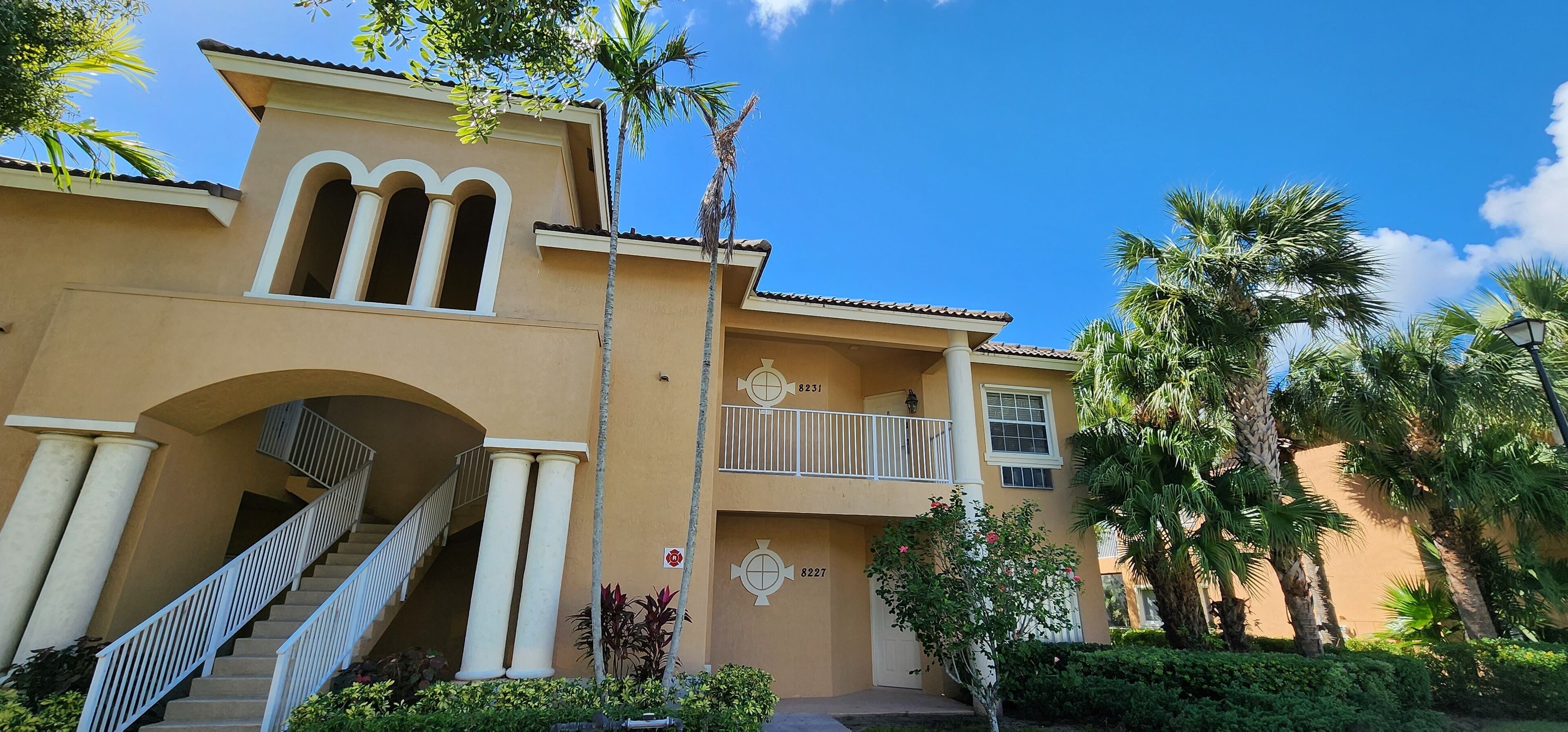 A multi-story building with a central staircase, balconies, and palm trees.