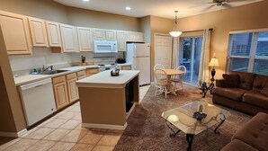 A modern kitchen with a central island, a dining area with chairs, and a living room with a sofa and a coffee table. - Right Direction Rentals (Port Saint Lucie)