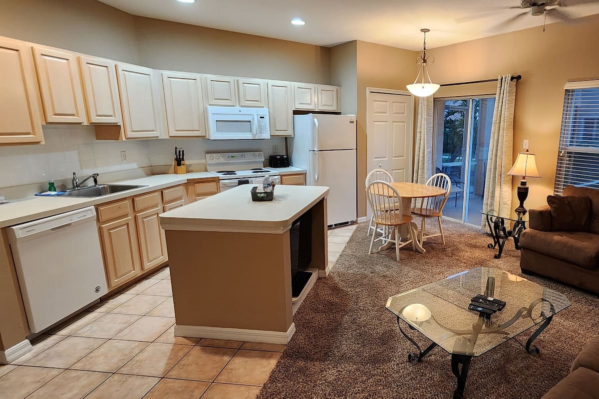 A modern kitchen with a central island, a dining area with chairs, and a living room with a sofa and a coffee table.