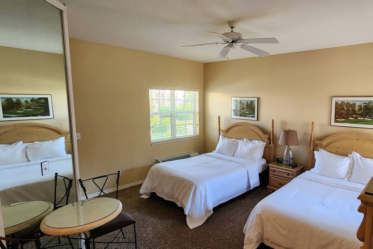 A hotel room with two beds, a ceiling fan, a small table, and a chair.
