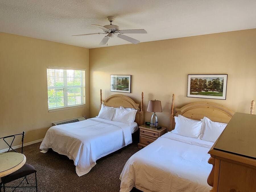 Habitación de hotel con dos camas, ventilador de techo, una mesita y una silla.