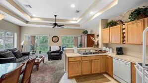 A modern kitchen with wooden cabinets, a dishwasher, and a dining area with a table and chairs. - Right Direction Rentals (Port Saint Lucie)