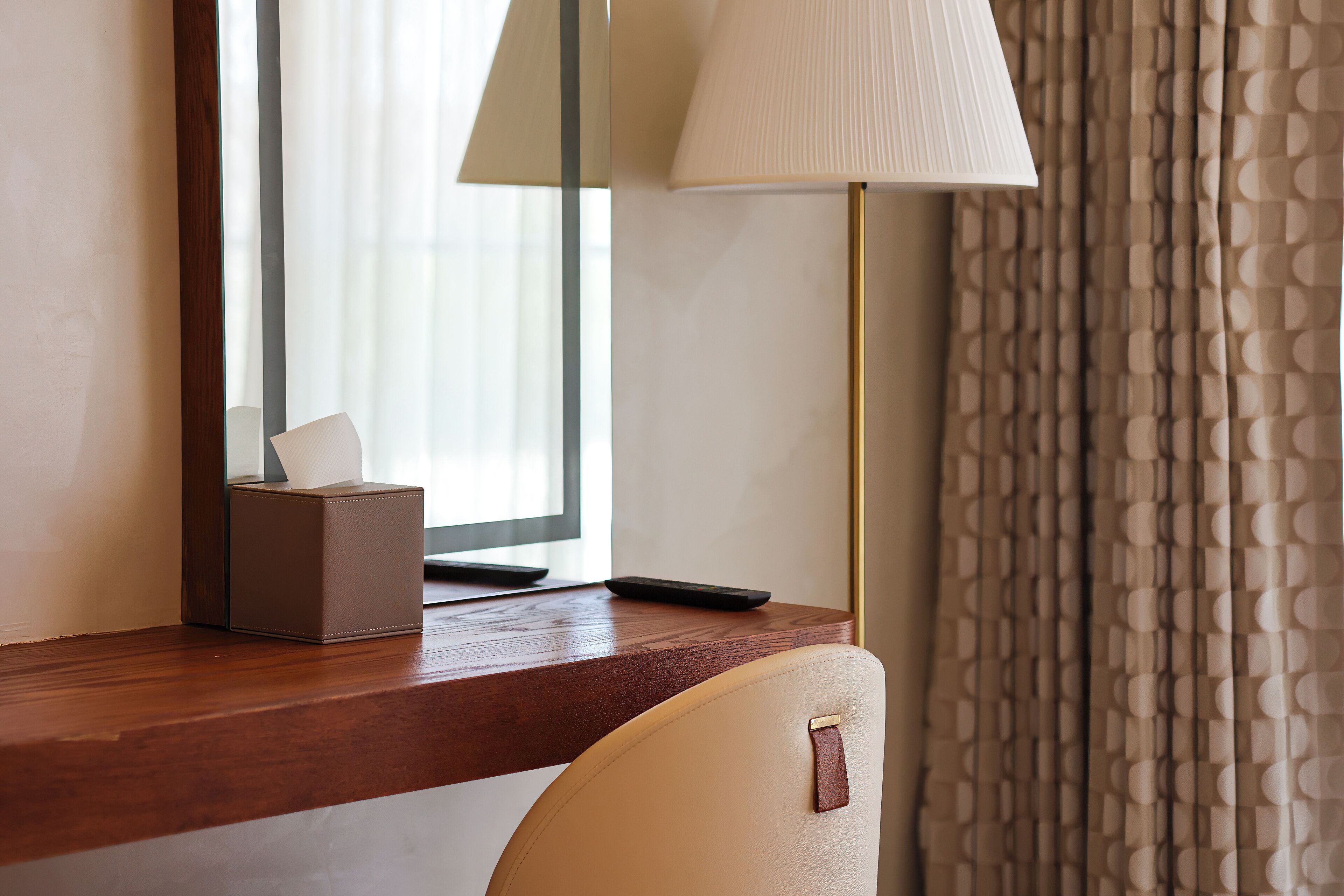 A hotel desk with a tissue box, remote control, and a lamp.