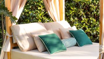 Una cama con múltiples almohadas y dosel, frente a un fondo de frondosa vegetación.