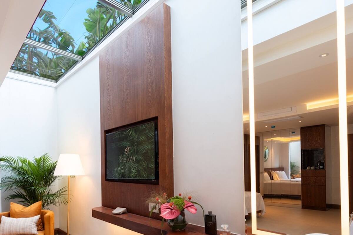 A modern hotel room with a large window, a wooden desk, a comfortable armchair, and a bed with a view of the outdoors.