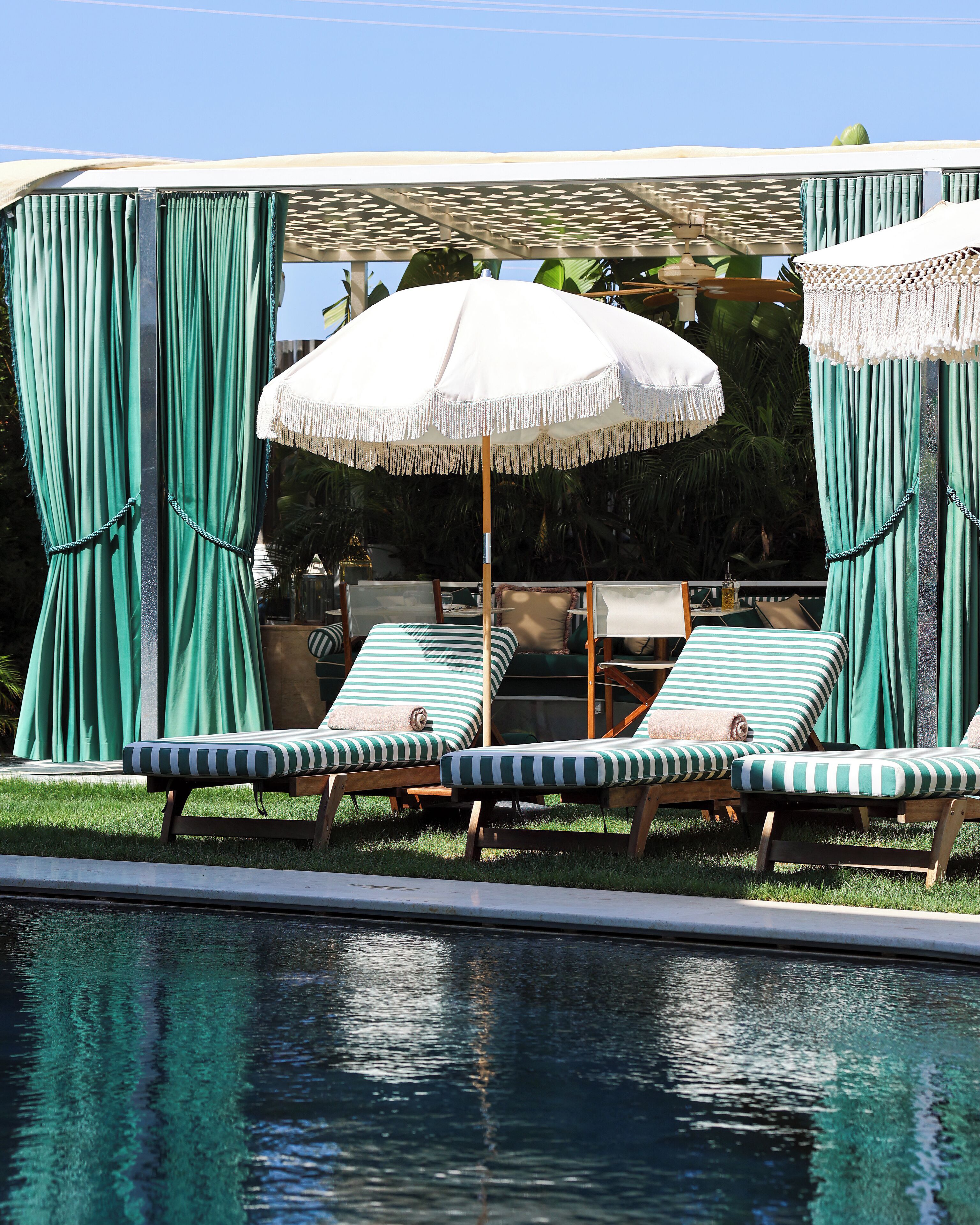 Zona junto a la piscina con sillones de descanso, una pérgola y cortinas.