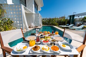 Una mesa de comedor con alimentos para el desayuno y vista a la piscina.