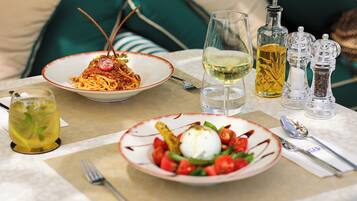 A dining table with two plates of pasta and a salad, a glass of white wine, and a bottle of olive oil.