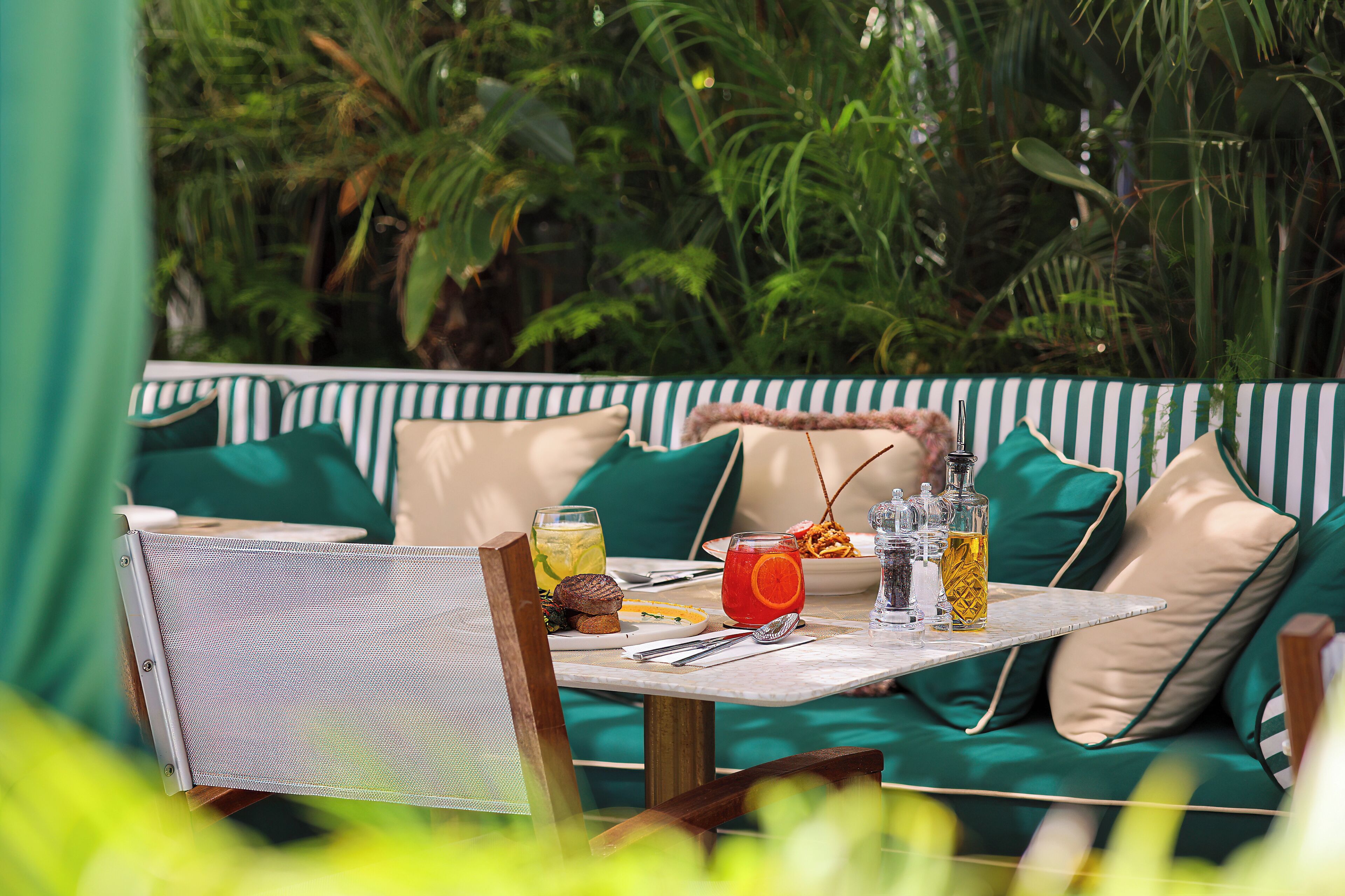An outdoor dining area with a table set for two, surrounded by green cushioned seating.