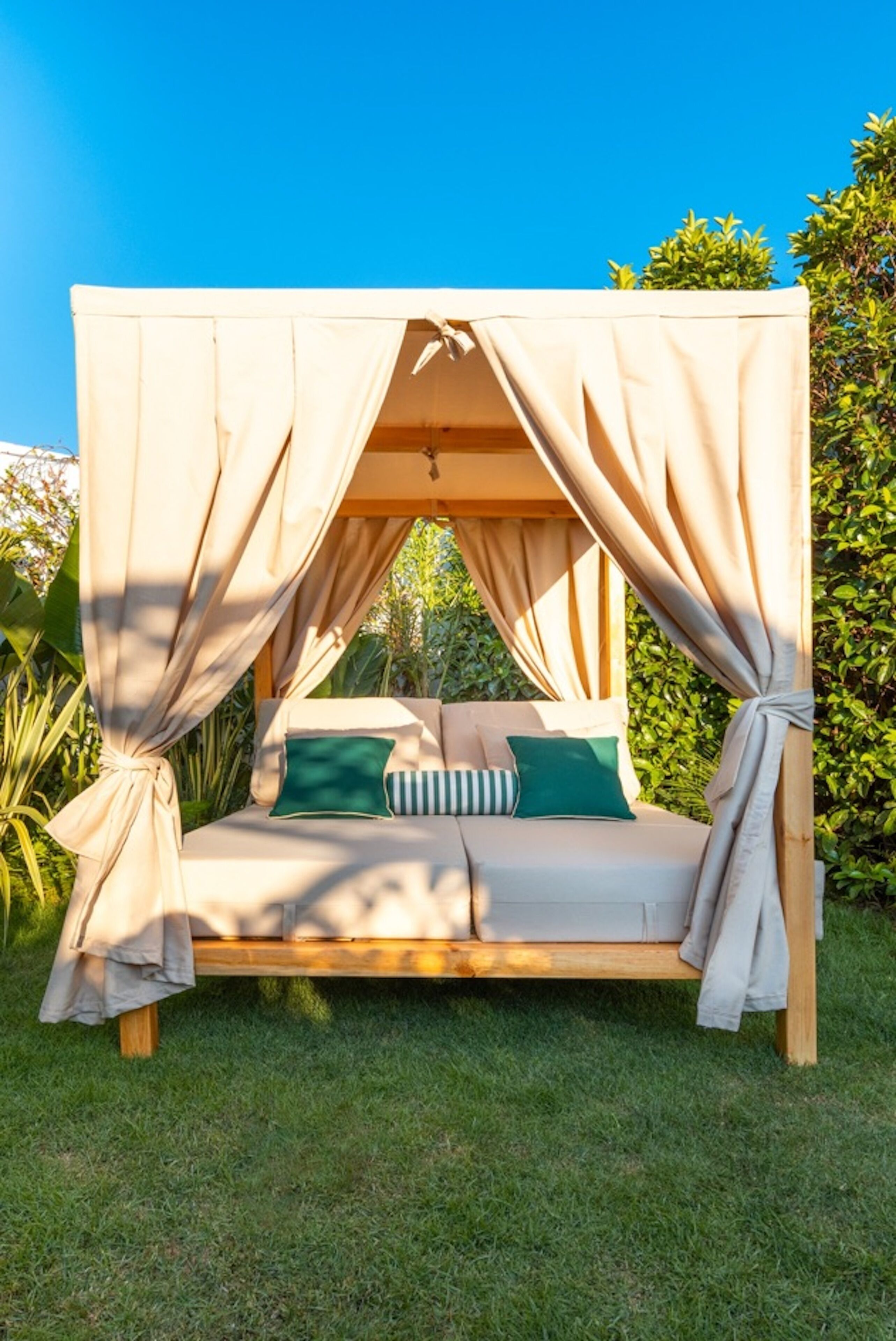 A wooden bed with a canopy, green and white striped pillows, and a beige blanket.