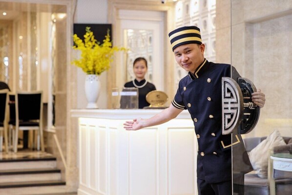 A hotel reception area with a receptionist, a reception desk, and a decorative vase with yellow flowers. - Classy Boutique Hotel (Hanoi)
