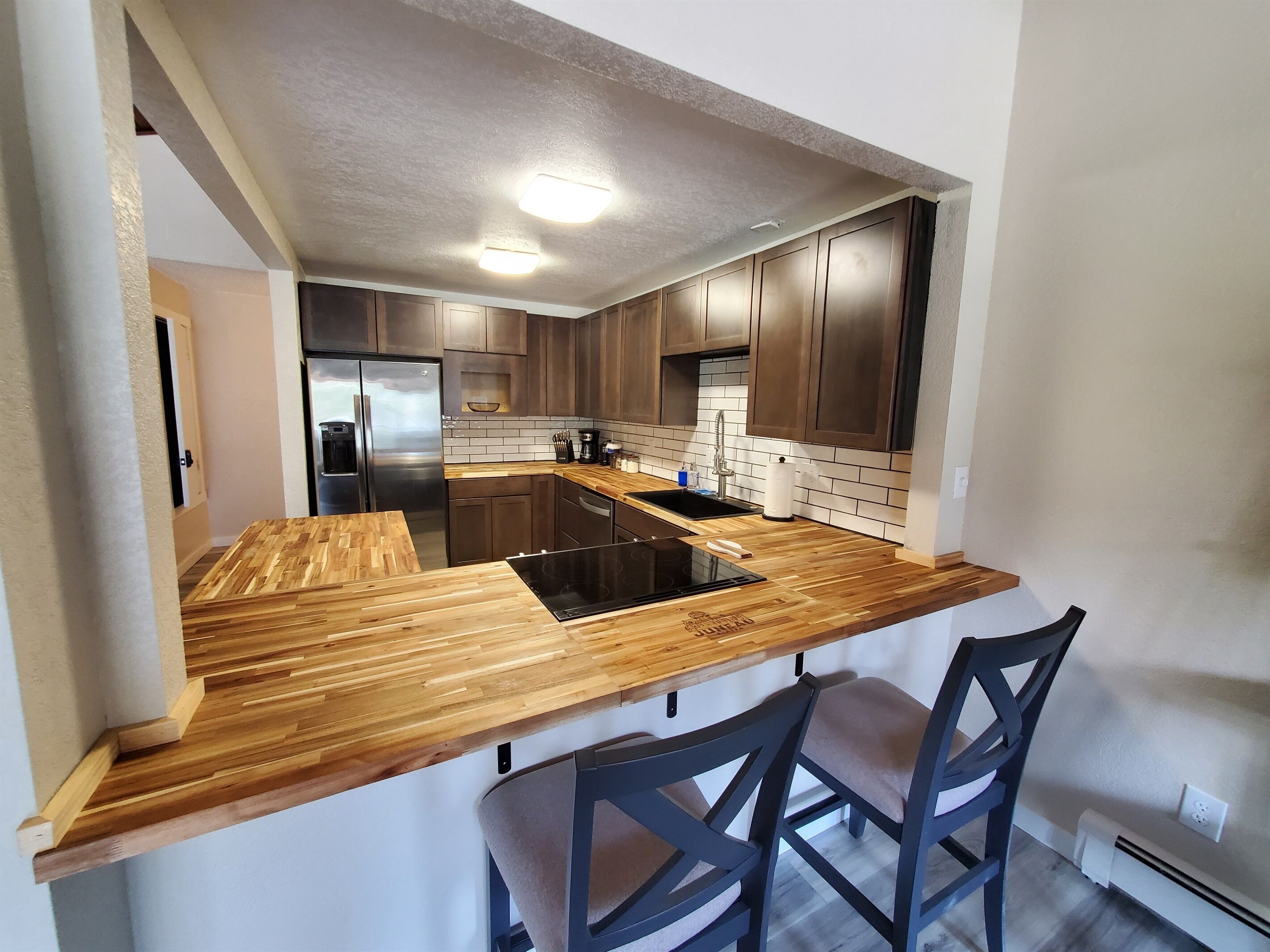 Une cuisine moderne avec des plans de travail en bois, un réfrigérateur en acier inoxydable et des meubles de cuisine en bois foncé.