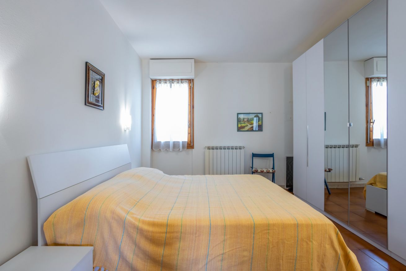 A bedroom with a bed, a radiator, a window with curtains, a framed picture, and a wardrobe.