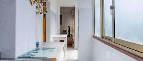 Una cocina estrecha con un ventanal grande, azulejos blancos y un lavamanos de acero inoxidable.