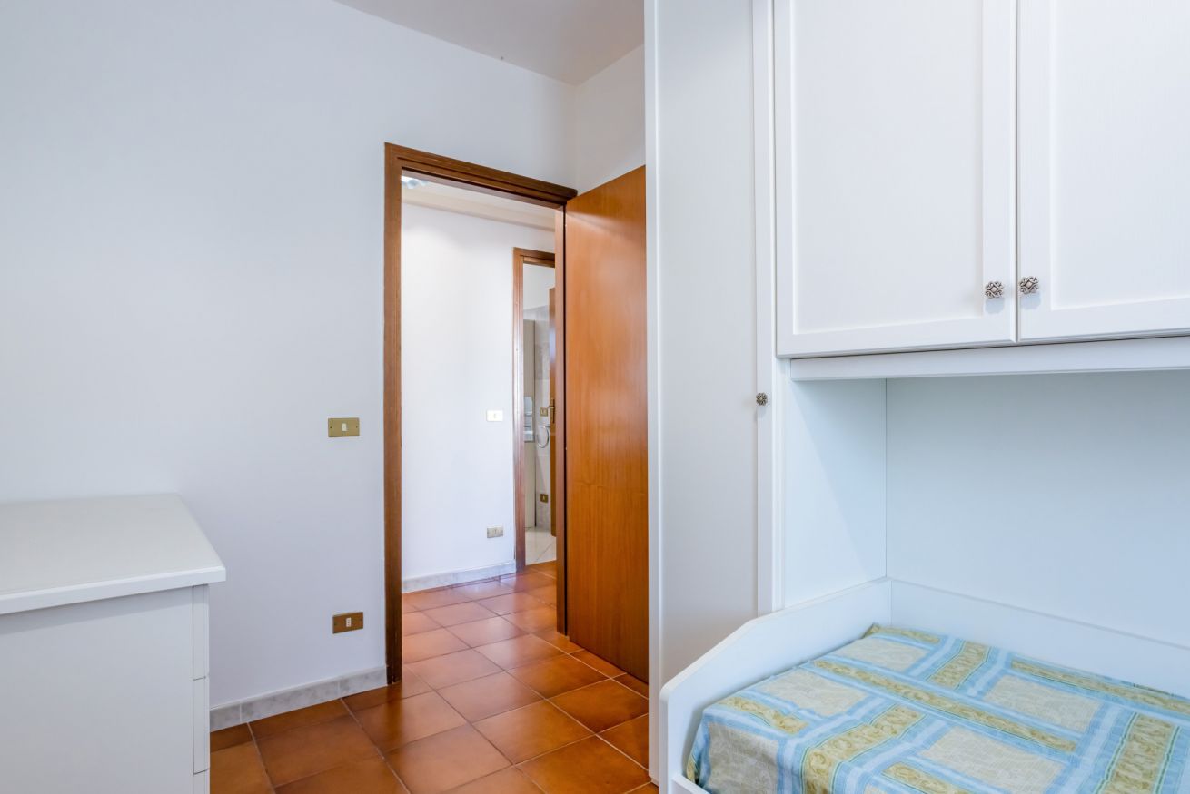 A room with a bed, a wardrobe, a white cabinet, and a tiled floor.