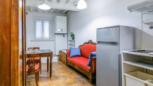 Een compacte keuken met een eettafel, een bank, een koelkast en een raam met daglicht.