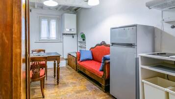 Ett kompakt kök med ett matbord, en soffa, ett kylskåp och ett fönster som släpper in naturligt ljus.