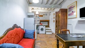 Een klein woongedeelte met een bank, een tafel, een wasmachine en een trap naar een verdieping erboven.