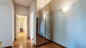 Een hal met houten vloer, een spiegelwand en een deur naar een andere kamer.
