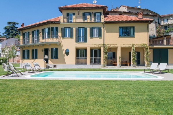 Un edificio de dos pisos con piscina, mobiliario exterior y un césped bien cuidado.