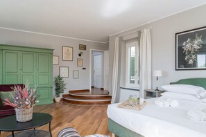 Una habitación de hotel con una cama, una mesita de noche, un armario verde y una silla, con un cuadro en la pared y una escalera que lleva a otra habitación.